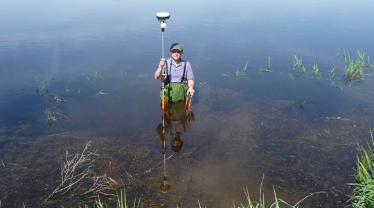 Ein Vermesser steht mit GNSS-Empfänger bei seiner Arbeit in einem Gewässer.
